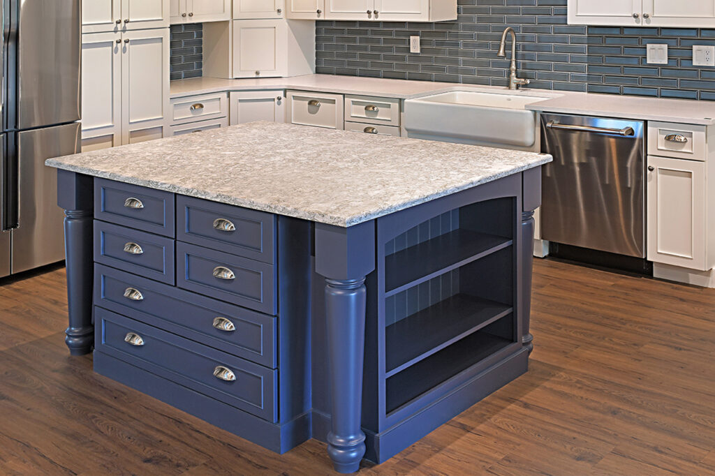 Blue kitchen island with multiple drawers and a speckled stone countertop in a modern kitchen surrounded by white cabinets and stainless appliances