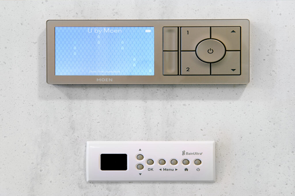 Moen U by Moen digital shower control with blue patterned touchscreen and circular right side control pad on a speckled wall